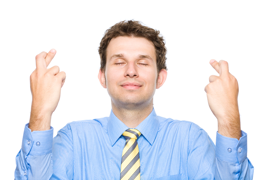 young man in a shirt and tie crossing his fingers, looking hopeful